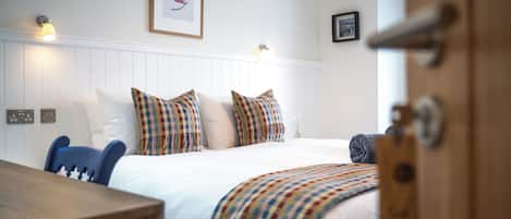 A neatly made bed with checkered bedding, a white headboard, and a framed leaf artwork above.