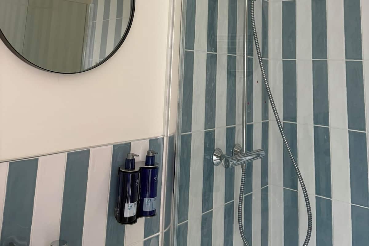A bathroom with a round mirror, a shower with a glass door, and striped tiles.