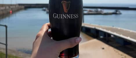 A hand holding a Guinness glass with a view of a body of water and a dock in the background.