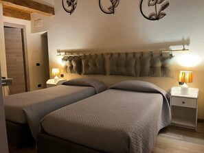 A bedroom with two beds, a wooden ceiling, decorative wall art, and bedside lamps.