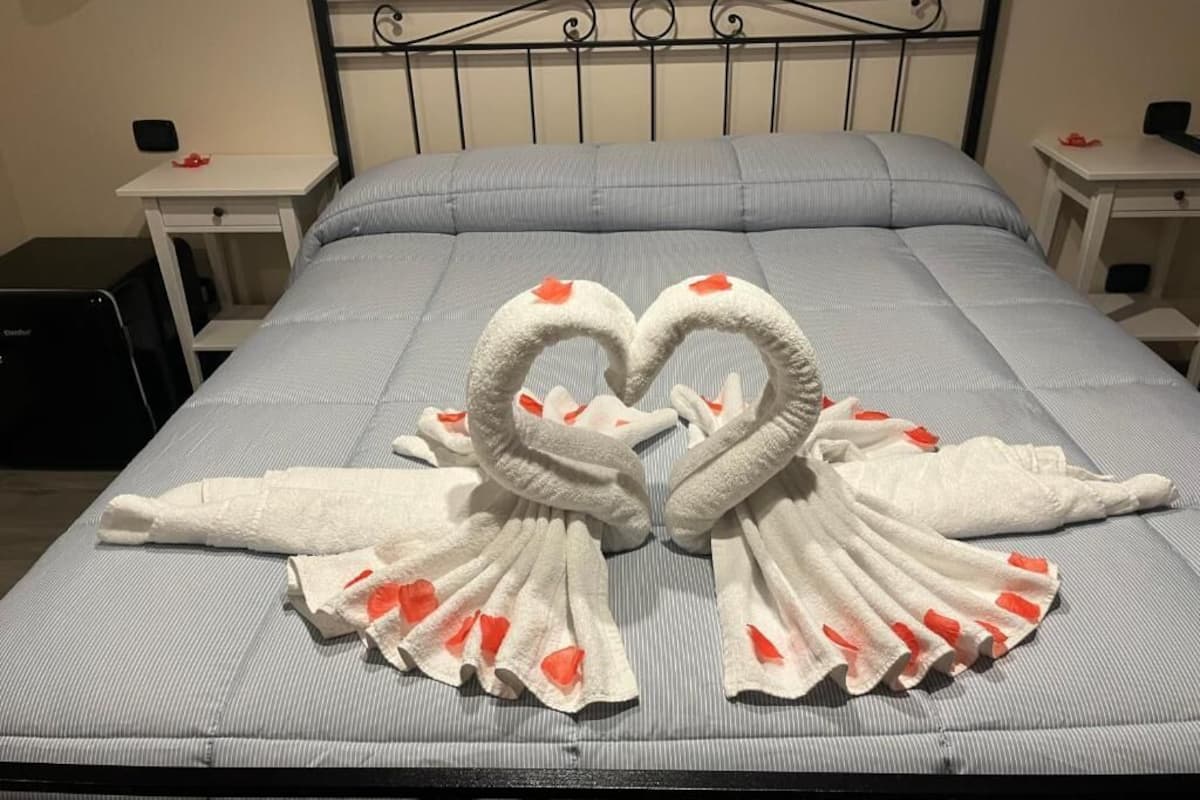 A bed with a heart-shaped towel arrangement and a plain wall.