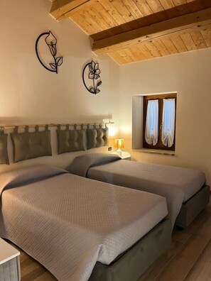 A room with two beds, a wooden ceiling, a window with curtains, and wall art.