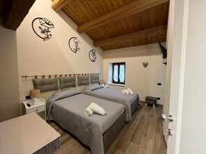 A bedroom with two beds, a wooden ceiling, a window, and a nightstand with a lamp.