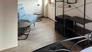 A compact room with a wooden ceiling, a sofa, a small table, a metal shelf with shoes, and a window. - Sibilroom - Rooms & Wellness (Amandola)
