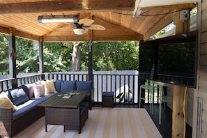 A covered patio with a sofa, table, and chairs, a ceiling fan, and a television.
