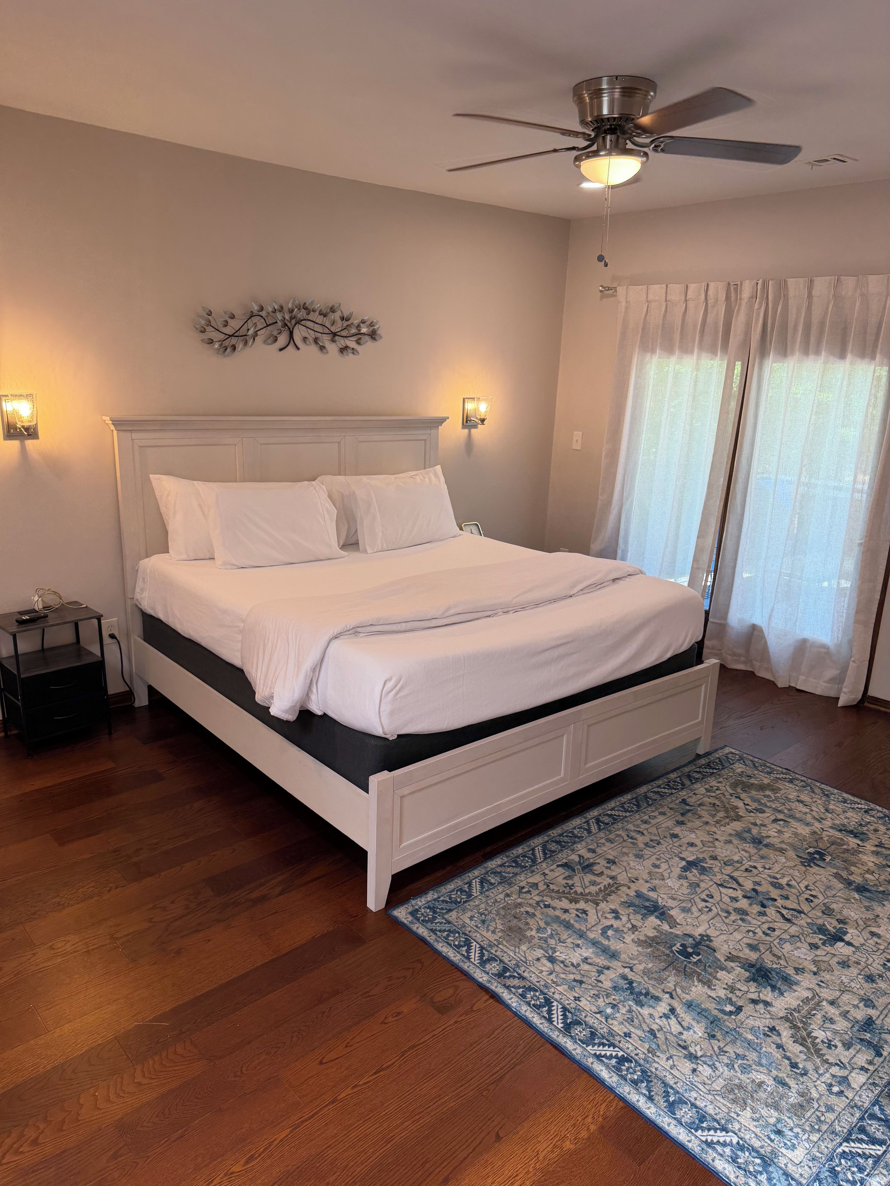 Une chambre à coucher avec un lit, un ventilateur de plafond, une table de chevet et un tapis à motifs.