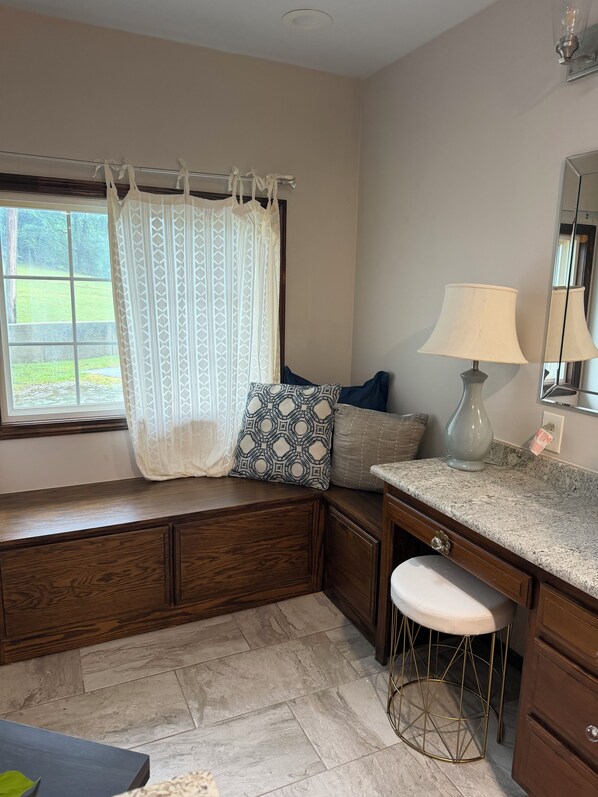 A bathroom with a window, a sink, a mirror, and a stool.