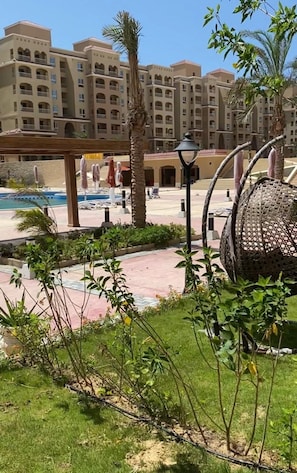 A hotel courtyard with a pool, palm trees, and a covered seating area. -   شاليه عائلي فاخر  بجاردن في AquaView – أكوافيو (elhammam)