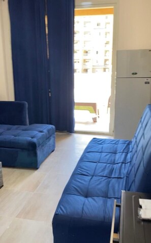 Une pièce comprenant un canapé, un fauteuil, un meuble et une porte donnant sur un espace extérieur.