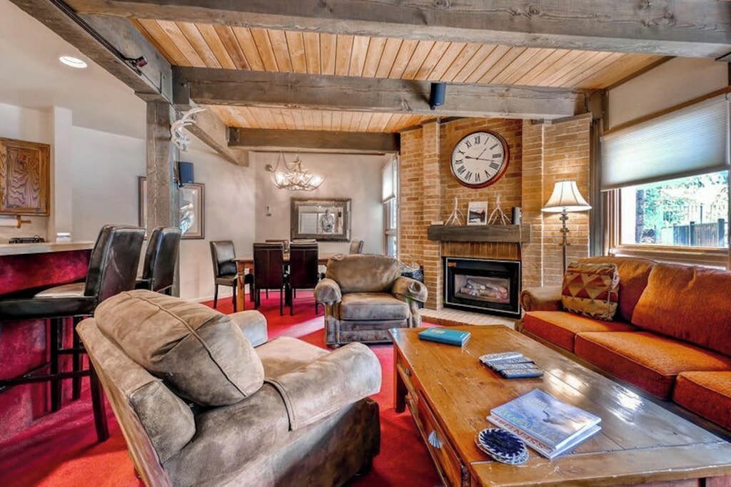 A cozy living room with leather sofas, a wooden coffee table, a fireplace, and a large clock on the wall.