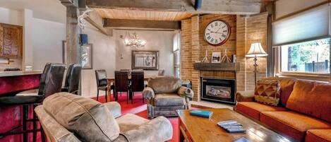 A cozy living room with leather sofas, a wooden coffee table, a fireplace, and a large clock on the wall.