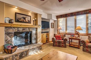 Una sala de estar con chimenea de piedra, muebles con diseños y un televisor.