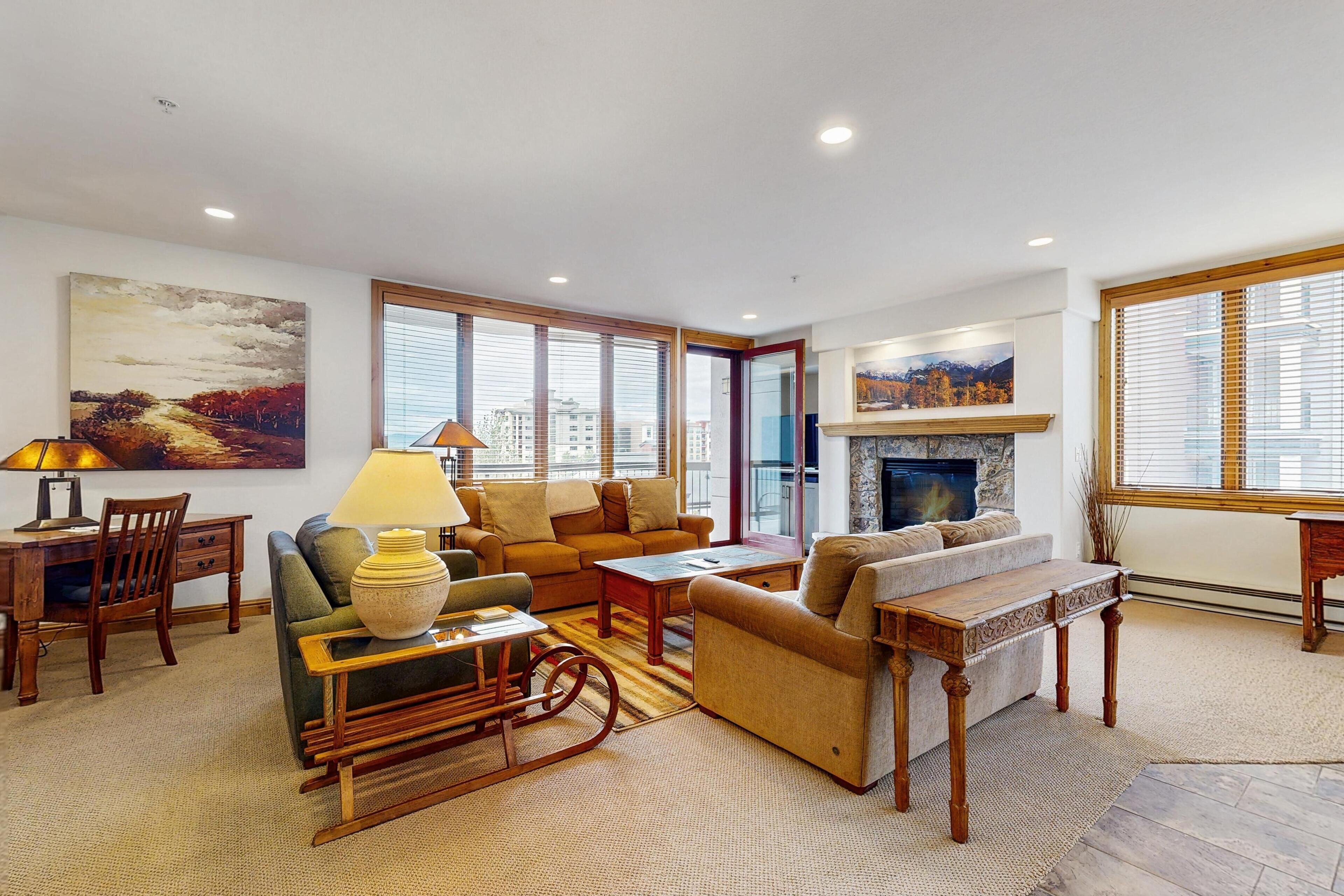 A spacious living room with a fireplace, comfortable seating, and large windows.