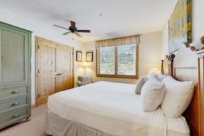 Um quarto com uma cama, um ventilador de teto, uma janela com persianas, uma luminária e um guarda-roupa.
