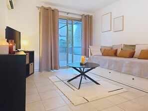 Ein modernes Wohnzimmer mit einer Couch, einem Couchtisch, einem Fernseher und einem Fenster mit Vorhängen.