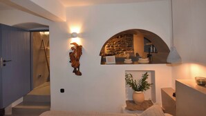 A modern interior with a stone archway, a wooden wall decor, a potted plant, and a staircase. - Katoi Suite, Vivian Suites Tinos (Tinos)