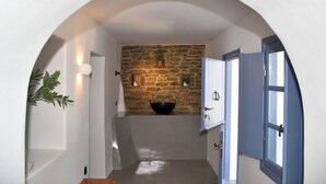 A narrow hallway with a stone wall, a black bowl on the wall, and a door with blue shutters. - Katoi Suite, Vivian Suites Tinos (Tinos)