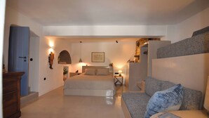 A bedroom with a bed, a sofa, a dresser, and a stone fireplace. - Katoi Suite, Vivian Suites Tinos (Tinos)