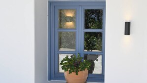 A window with a blue frame, a potted plant, and a cushion on a white bench. - Katoi Suite, Vivian Suites Tinos (Tinos)