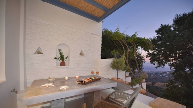 Un área de comedor al aire libre con una mesa de piedra, sillas de mimbre y vistas al paisaje.