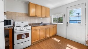 A kitchen with wooden cabinets, a white stove, a microwave, and a window with a view of the outdoors. - Relaxing Countryside Stay (Bailieboro)