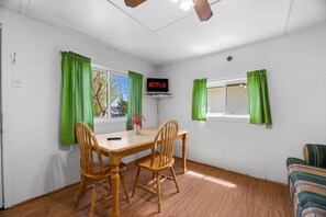 A room with a wooden table and chairs, a TV mounted on the wall, and green curtains. - Relaxing Retreat | Near Lakes (Bailieboro)