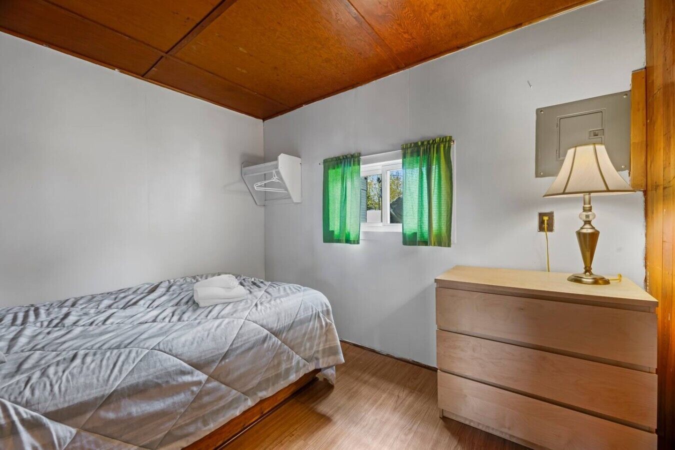 A bedroom with a bed, a dresser, a window with curtains, and a lamp.