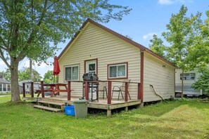 A single-story house with a porch, a barbecue grill, and a small table.