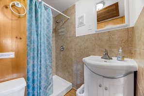 Un baño con ducha, inodoro, lavamanos y un espejo sobre el lavamanos.