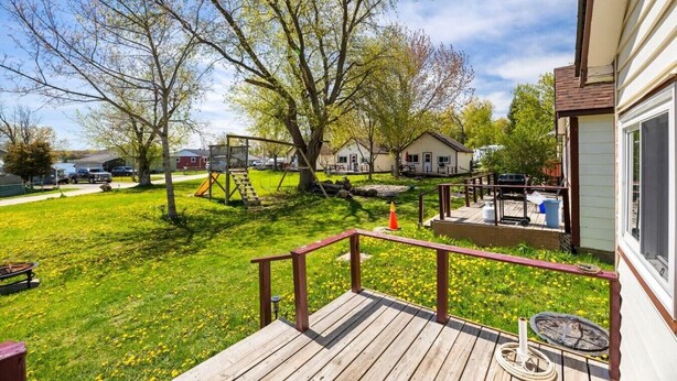 Eine Terrasse mit Geländer, eine Rasenfläche mit Bäumen und ein Spielplatz im Hintergrund.
