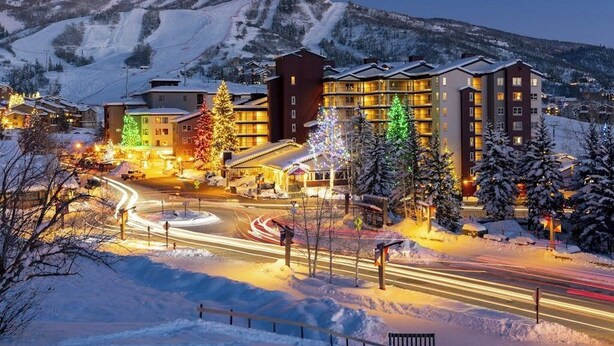 Un hotel de varios pisos, con una pista de esquí al fondo y un paisaje cubierto de nieve.