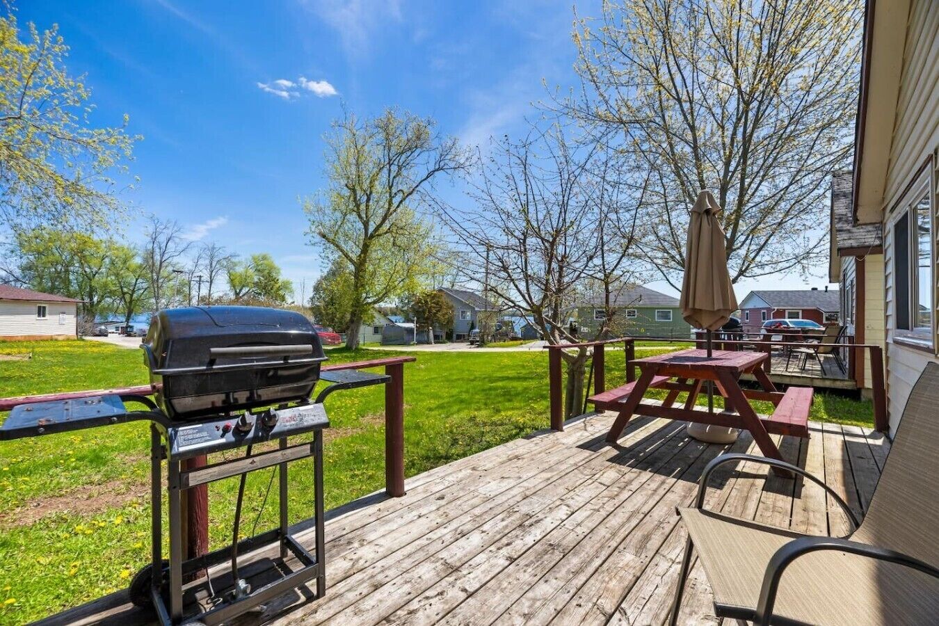 A wooden deck with a barbecue grill, picnic table, and umbrella.