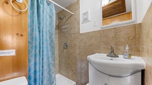 Een badkamer met een douche, toilet, wastafel en een spiegel boven de wastafel.