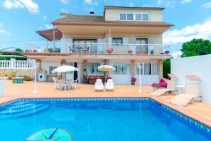 Ein zweigeschossiges Haus mit Swimmingpool, Gartenmöbeln und einem Balkon mit Blumentöpfen.