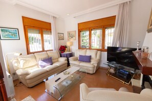 Ein Wohnzimmer mit zwei Sofas, einem Couchtisch, einem Fernseher auf einem Schrank und einem Fenster mit Vorhängen.
