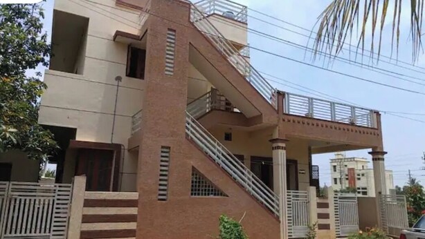 Un edificio moderno de dos pisos con una escalera, entrada protegida por una reja y un coche estacionado cerca.