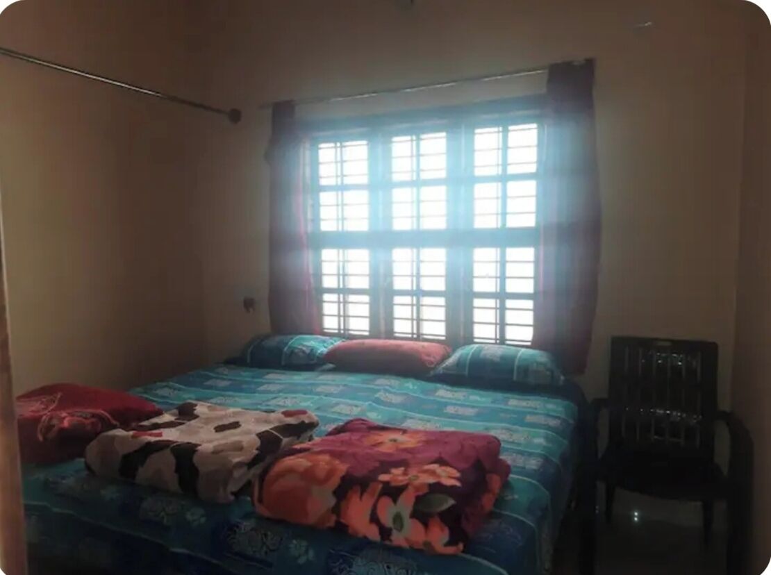 A bedroom with a bed, pillows, a chair, and a window.