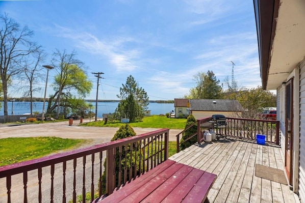A wooden deck with a railing, a barbecue grill, and a view of a lake.
