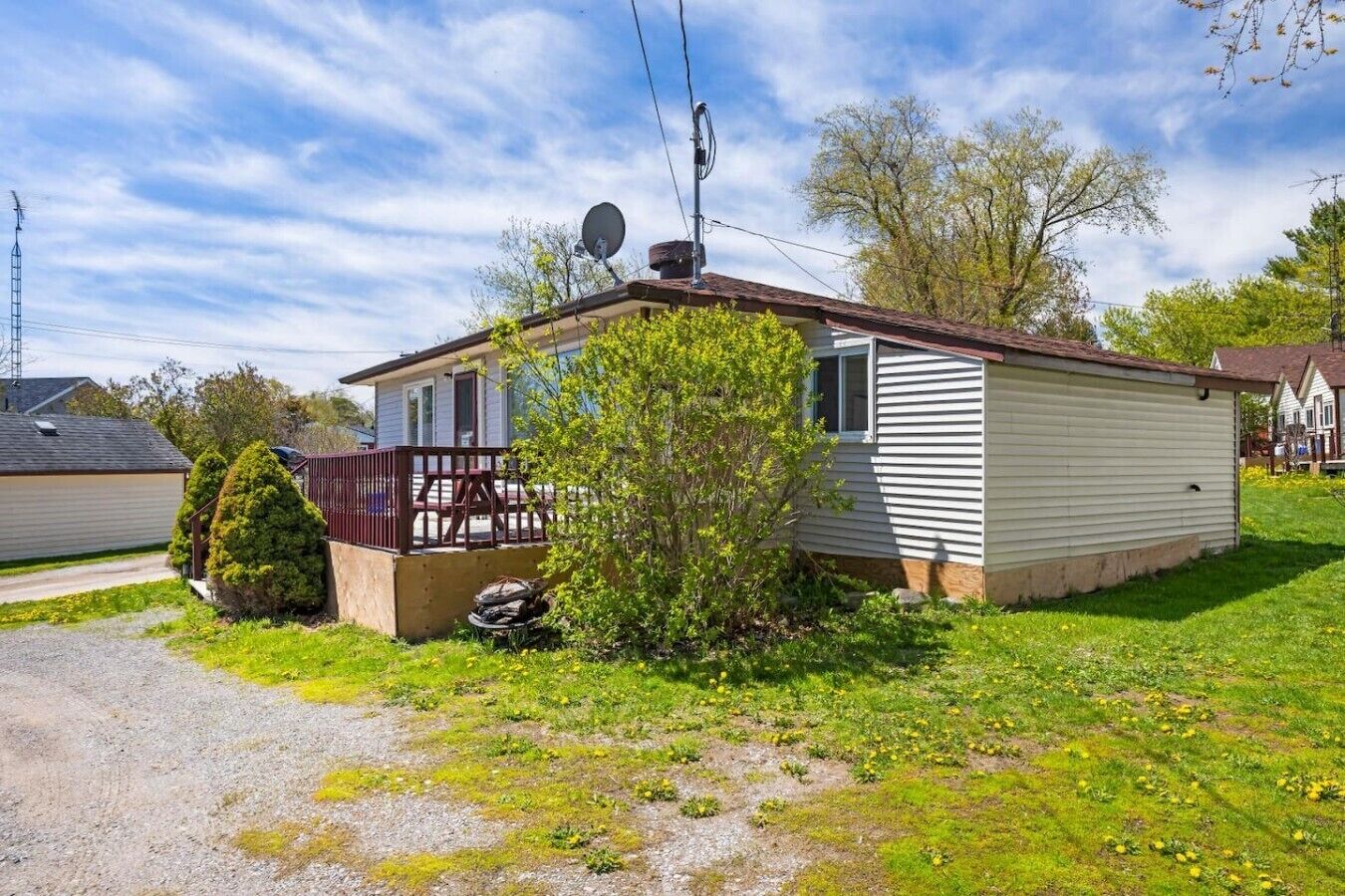 A single-story mobile home with a fenced porch, satellite dish, and a small yard with grass and shrubs.