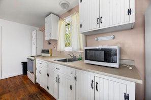 A kitchen with white cabinets, a microwave, a sink, and a window with curtains.