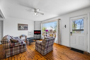A living room with plaid furniture, a ceiling fan, a TV, and a door with a sign.