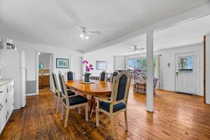 A spacious dining area with a wooden table and chairs, a ceiling fan, and a view of the outdoors.