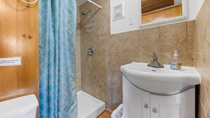 Et badeværelse med bruser, toilet, vask og et spejl over vasken.