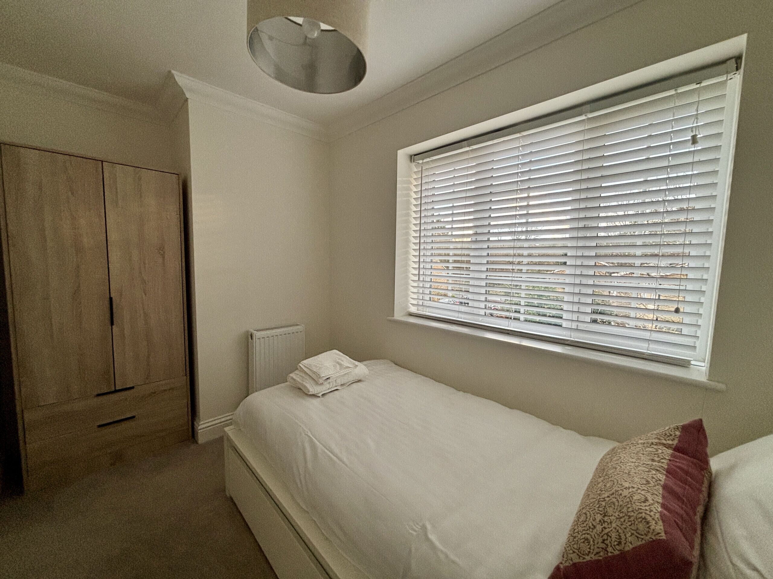 Un dormitorio con cama, ventana con persianas, radiador y armario.
