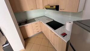 Eine kompakte Küche mit hellen Holzschränken, einer schwarzen Arbeitsplatte, einem Spülbecken und einem Kühlschrank.