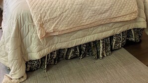 Un llit ben fet amb un mantell acolxat, una làmpada de nit i dos quadres florals a la paret.