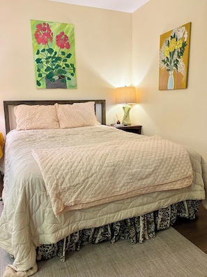 A neatly made bed with a quilted cover, a bedside lamp, and two floral paintings on the wall. - That 70s Bungalow - Pet Friendly! - studio with AC in charming Wilmington (Wilmington)