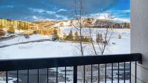 A snowy landscape with buildings, a clear sky, and a balcony railing. - Stylish ski-in/out condo w/views in base area next to gondola, pool & restaurant (Steamboat Springs)