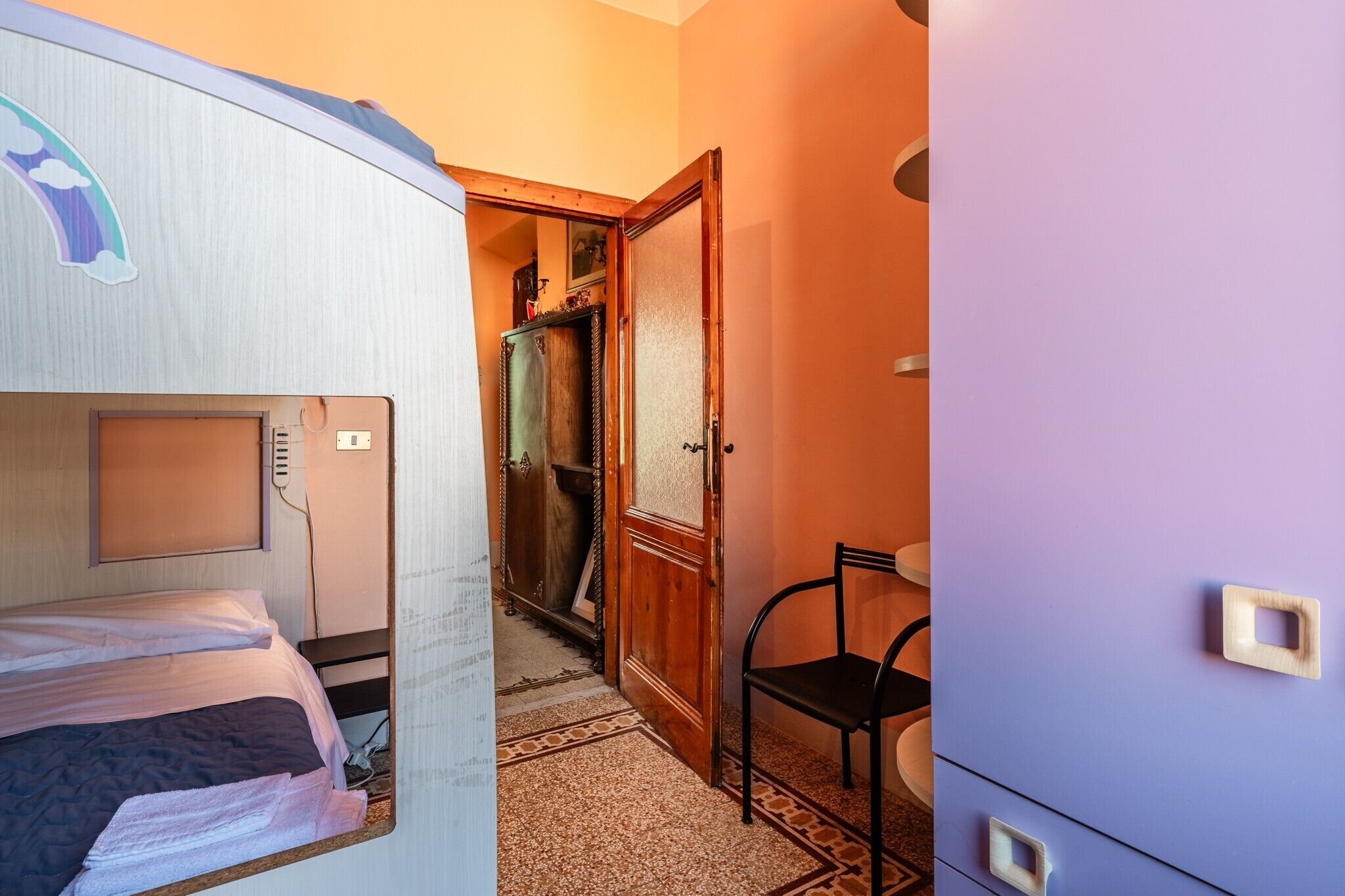 Une petite pièce comprenant un lit, une chaise, une armoire et une porte donnant sur une autre pièce.