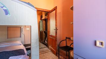 Une petite pièce comprenant un lit, une chaise, une armoire et une porte donnant sur une autre pièce.